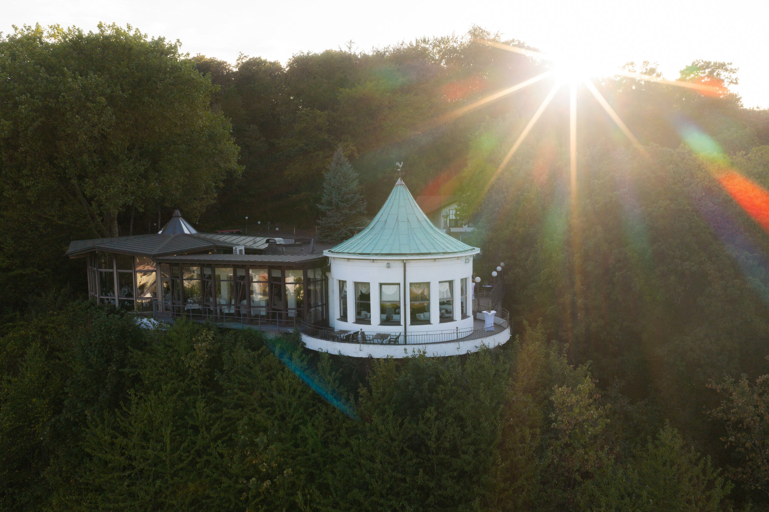 Die Villa Vue in Essen von oben in der Abendsonne: runder Anbau mit Kupferdach, ringsum Wald