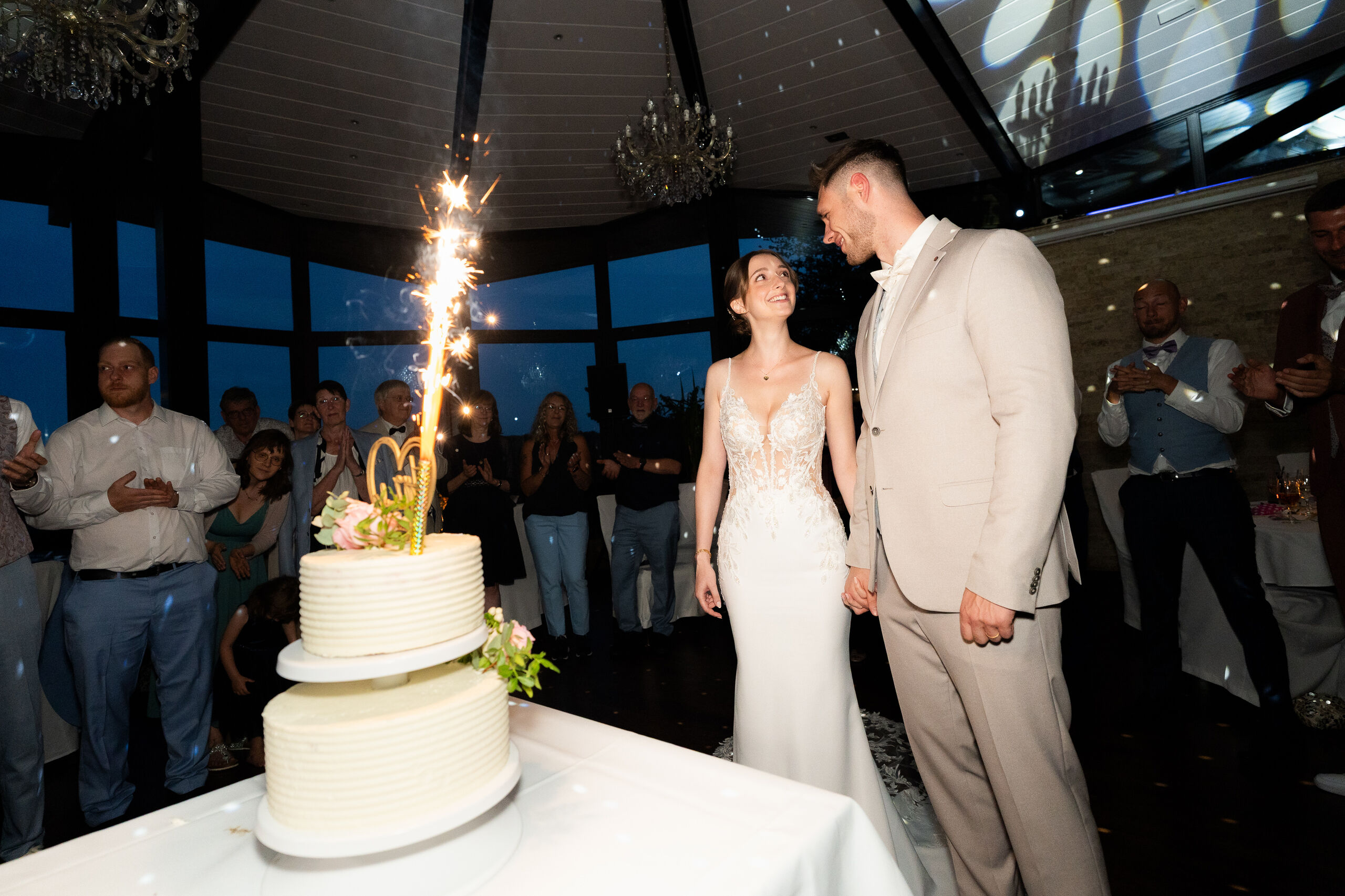Anschnitt der Hochzeitstorte mit Wunderkerze im Saal